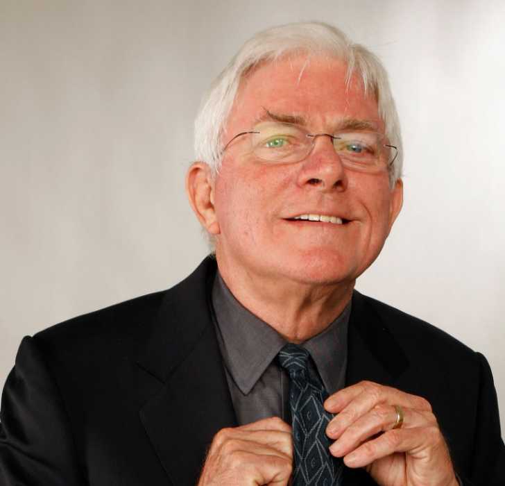 Picture of Phil Donahue posing for a photo in black suit holding his tie with both hands.